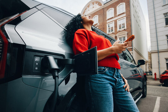 Young woman relaxes while fast charging electric car in city