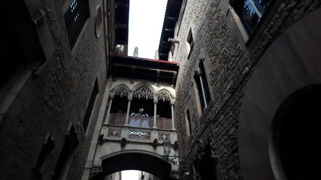 Upward view of the iconic pont del bisbe, a famous neo gothic archway connecting two historic buildings over a narrow alley in the atmospheric gothic quarter of barcelona, spain