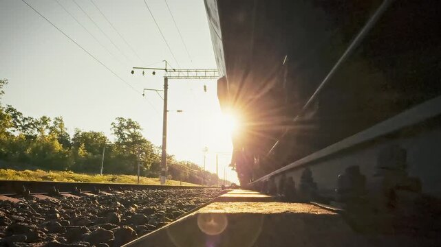 A freight train thunders across the countryside on iron rails, a close-up captures its rotating wheelsets. The shot highlights rapid logistics flow and the role of sustainable rail infrastructure