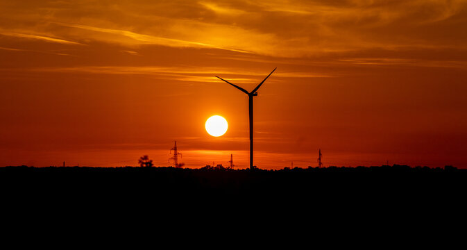 Wind turbine silhouette at sunset with orange sky and power lines