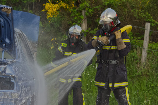 Two firefighters spraying water on burning car during rescue training exercise
