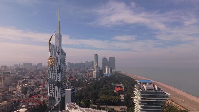 A smooth pull-back drone shot starts over the calm Black Sea, retreating to reveal the entire Batumi cityscape, its modern skyscrapers, and the vibrant coastal promenade.