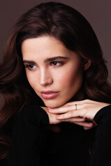Fototapeta premium A thoughtful woman with brunette hair poses in a beauty portrait wearing a black sweater. Soft studio lighting highlights natural makeup, smooth skin, expressive eyes against a warm background.