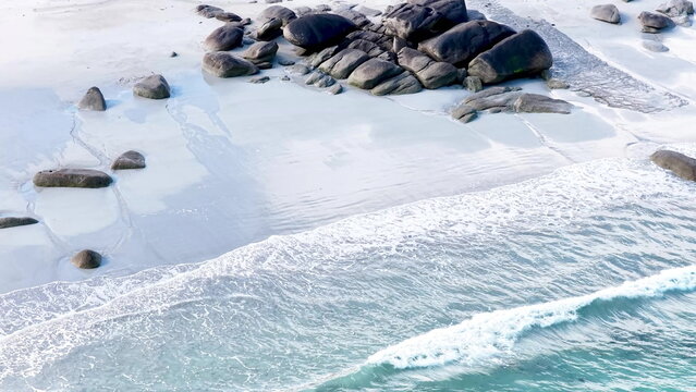 Eine beeindruckende Luftansicht vom Plage de Boutrouilles, bei der sanfte, wei&szlig;e Wellenmuster auf den hellen Sandstrand und die charakteristischen, dunklen Felsformationen treffen.