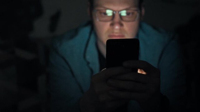 A man stares at his smartphone screen in a dim night room, the bright backlight highlighting his focused eyes. This digital addiction scene underscores how night gadget use disrupts sleep