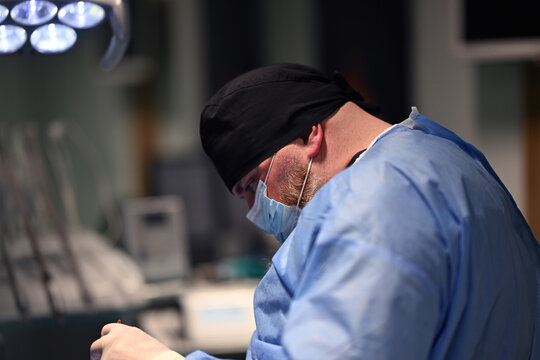 Surgeon Performing Operation in Modern Operating Room Wearing Surgical Mask and Scrubs