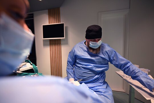 Bearded Surgeon in Mask and Scrubs Preparing Instruments in Modern Operating Room During Surgery