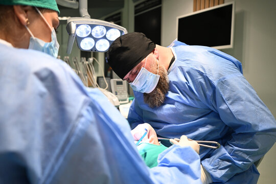 Oral Surgeon Performing Dental Surgery In Sterile Clinic With Surgical Team And Overhead Lights