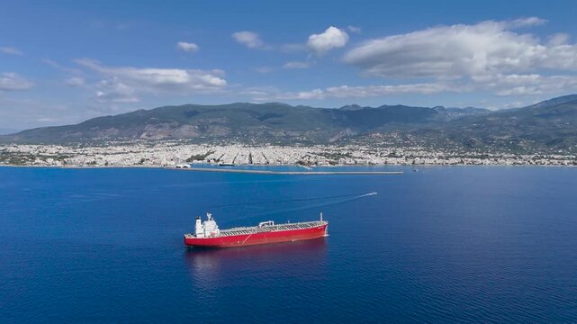 Aerial View of Red Cargo Ship Anchored off Kalamata Coast with Speedboat Wake, Harbor Breakwater, Coastal Cityscape and Taygetus Mountains in Greece