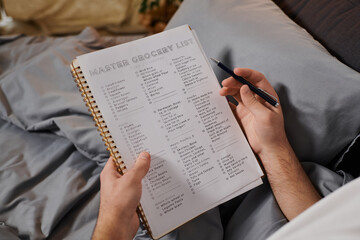 Naklejka premium Living with diabetes, a young man writes a grocery list in bed, balancing health and routine.