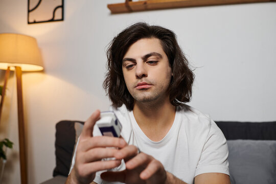Caucasian man with long hair checks his blood sugar levels in a modern apartment during morning.