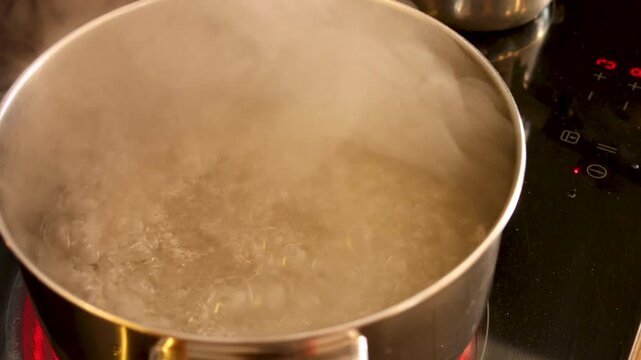 boiling water in pot for pasta cooking on stove with steam, water boiling in metal pot on stove with bubbles steam and heat during cooking process