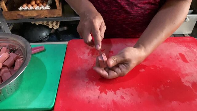 Hands slicing raw sausages on a cutting board A descriptive close-up stock footage clip showing a person's hands using a sharp kitchen knife to slice raw sausages into pieces on a cutting board. 