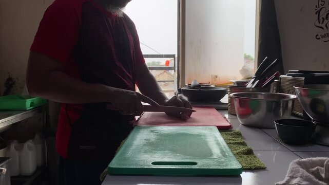 Hands slicing raw sausages on a cutting board A descriptive close-up stock footage clip showing a person's hands using a sharp kitchen knife to slice raw sausages into pieces on a cutting board. 