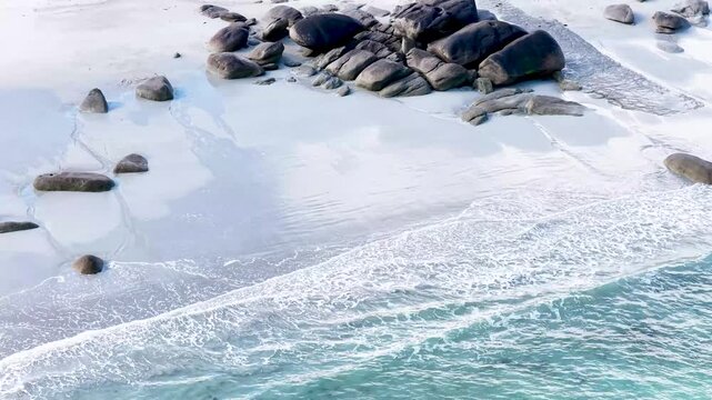 Eine beeindruckende Luftansicht vom Plage de Boutrouilles, bei der sanfte, wei&szlig;e Wellenmuster auf den hellen Sandstrand und die charakteristischen, dunklen Felsformationen treffen.