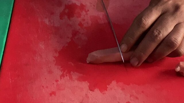 Hands slicing raw sausages on a cutting board A descriptive close-up stock footage clip showing a person's hands using a sharp kitchen knife to slice raw sausages into pieces on a cutting board. 