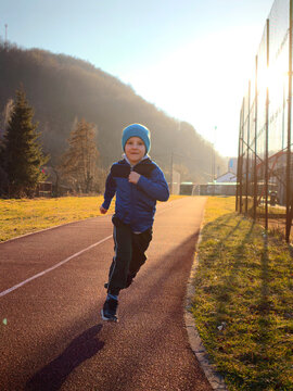 Young Boy Running on Outdoor Track at Sunset Wearing Blue Jacket and Beanie