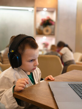 Focused Young Boy Wearing Headphones While Using Laptop at Cafe Table for Online Learning