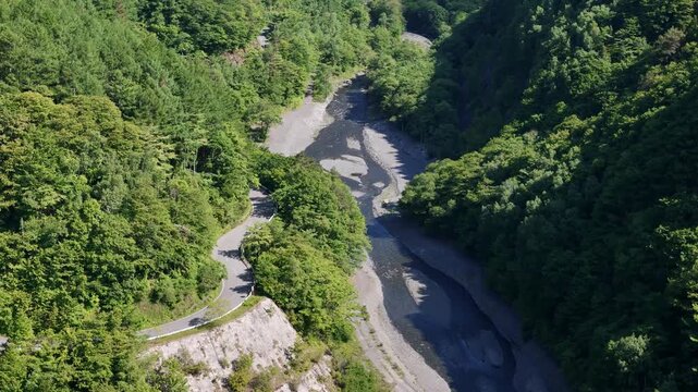 Aerial view captures winding river through lush green valley. Rocks and gravel beds reveal river's natural flow and depth. Foggy light enhances the serene, untouched forest atmosphere
