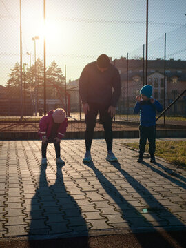 Father Exercising Outdoors With Two Children at Sunset on Urban Playground Pavement