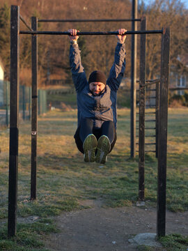 Outdoor Fitness Man Doing Hanging Leg Raise on Pull-Up Bar in Cold Park Workout Session