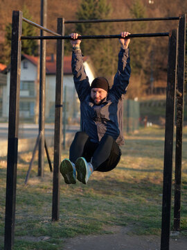 Man Doing Outdoor Pull-Up Leg Raise Workout on Metal Bar in Park During Cold Weather