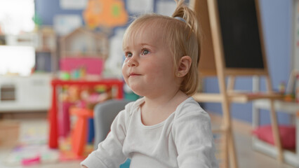 Obraz premium Toddler girl covering face with hands playing peekaboo amid colorful toys in daycare building; playful curiosity.