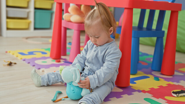 Toddler girl holding plush elephant toy seated on foam puzzle mat in building; gentle curiosity calm.