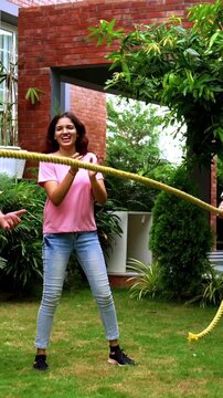 Indian kids playing tug of war or rassi khech in home garden while parents cheer them, spending quality fun time together enjoying traditional outdoor sports bonding during weekend family activity