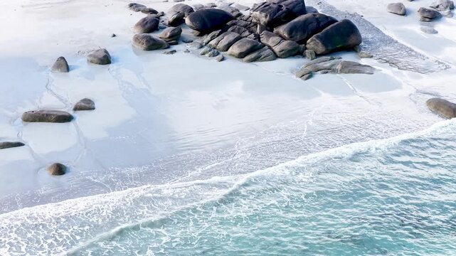 Eine beeindruckende Luftansicht vom Plage de Boutrouilles, bei der sanfte, wei&szlig;e Wellenmuster auf den hellen Sandstrand und die charakteristischen, dunklen Felsformationen treffen.