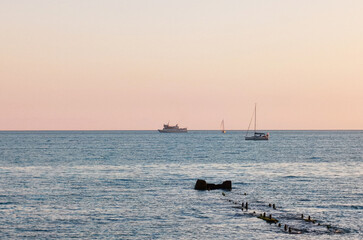 Obraz premium A white yacht and a ship with a mast sail across the sea against a blue sky at sunset