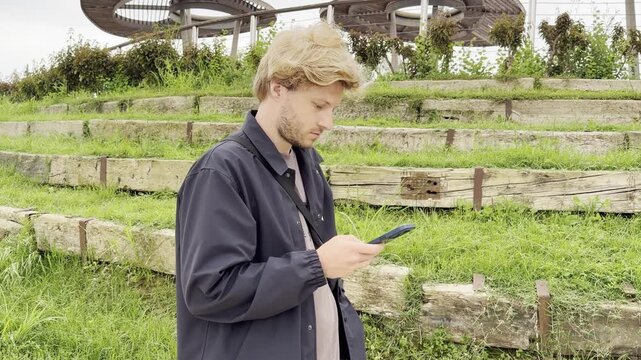 Lifestyle portrait of young man using a smartphone outdoors.Man  type message on smartphone in summer  city park. 