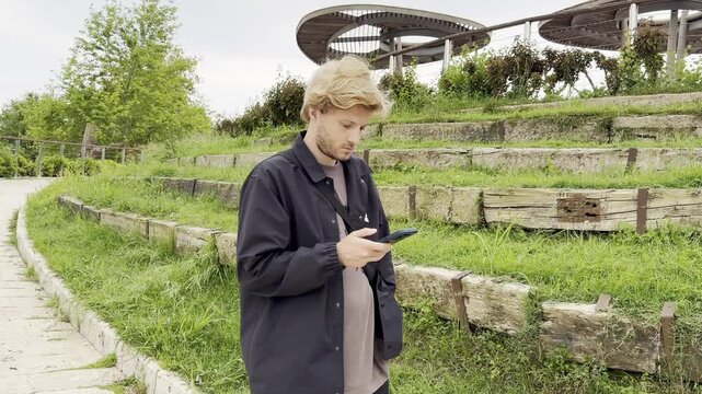 Lifestyle portrait of young man using a smartphone outdoors.Man  type message on smartphone in summer  city park. 