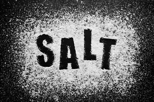 Word salt stenciled in white sea mineral powder on black background representing essential culinary ingredient