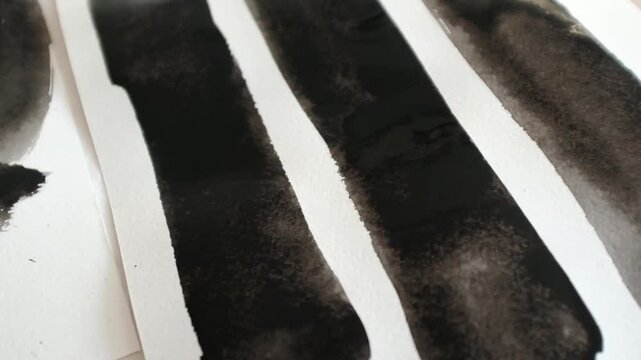 close-up shot capturing a hand using a round mop brush to create a bold, abstract ink painting on textured white paper, it absorbs the ink, showcasing realistic bleeding and dry brush strokes. 