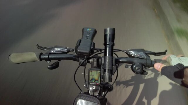 Man holding bicycle handlebar while riding outdoor in nature POV cycling on smooth road surface with visible handlebars representing steady riding and travel flow