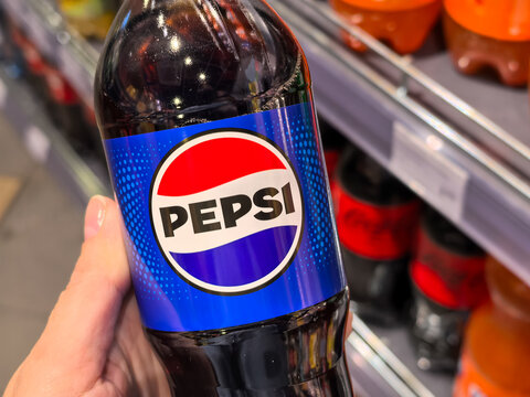 Hand holding Pepsi cola plastic bottle in supermarket store aisle