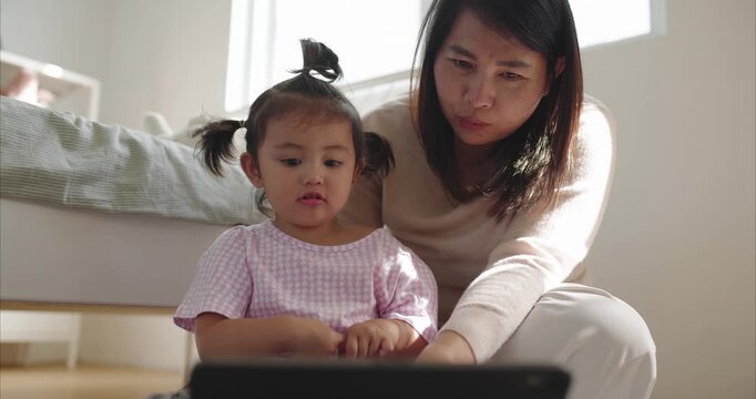 Asian Mother and Two Year Old Toddler Girl using Tablet on Floor Together morning light	