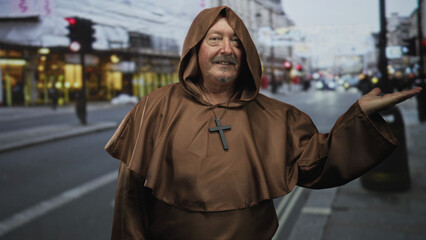 Obraz premium Senior man monk in brown robe with cross necklace presents open palm on a street; serenity welcome hospitality.