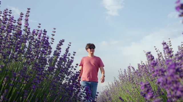 Lavender field man walking summer purple countryside travel outdoor nature along rural farm path under blue sky, casual style with sunglasses, watch, joyful mood, fragrant bloom lining narrow trail