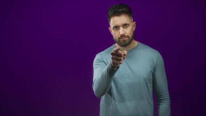 Obraz premium Hispanic man with beard pointing finger at camera in studio with purple backdrop; direct confidence.