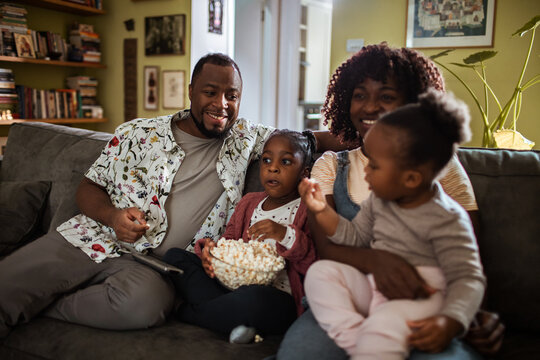Smiling parents and kids watching tv at home