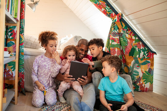 Father and children using tablet in cozy attic playroom