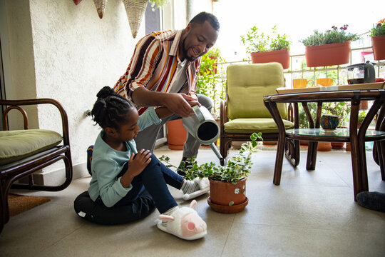 Father and daughter watering balcony plants at home