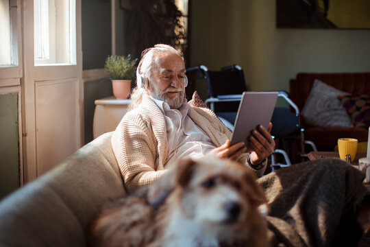 Senior man with headphones using tablet on sofa at home