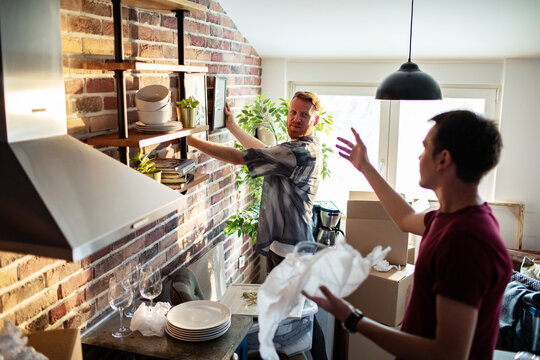 Two men unpacking dishes and arranging kitchen shelves at home