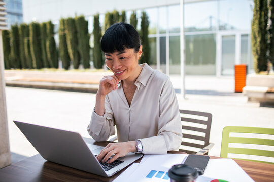 Smiling businesswoman working on laptop in outdoor office courtyard