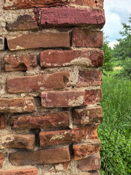 Crumbling old red brick pillar edge with green meadow in background