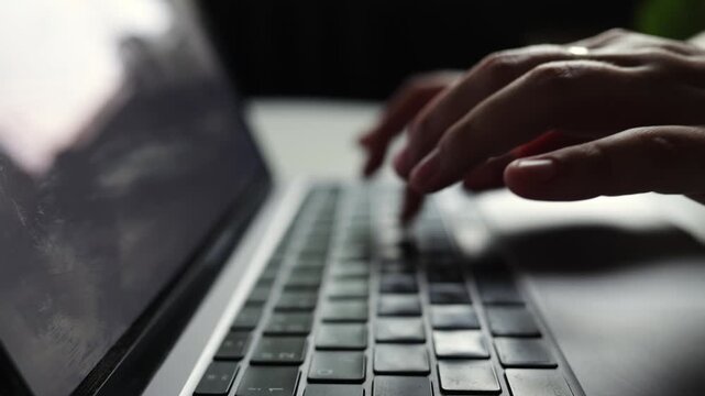 Close-up of hands typing on a laptop keyboard in dim lighting