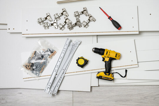 Top view of furniture assembly parts including electric screwdriver power drill metal hinges slides screws and white boards repair and renovation concept flat lay, IY home .
